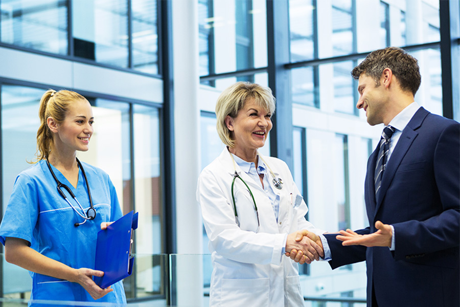 Two nurses shake hands with a business person