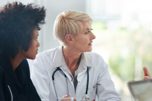 A person wearing a white medical coat listens to someone speaking.
